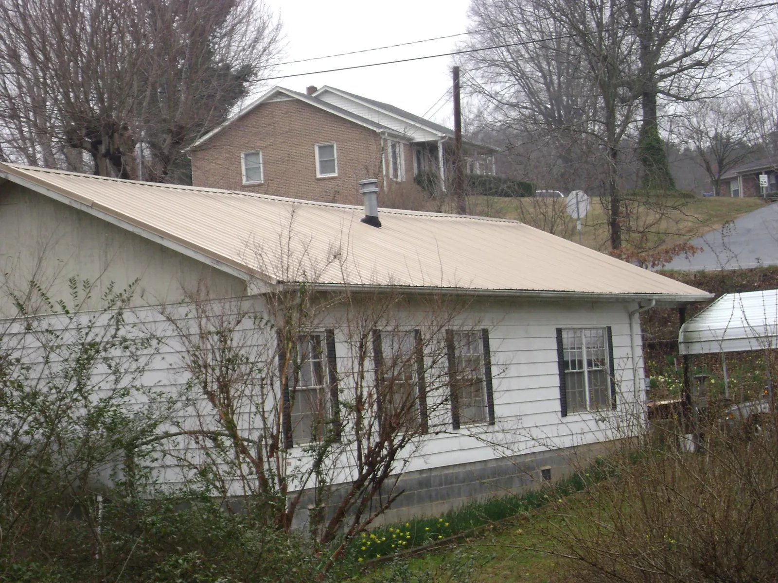 Tan metal roof on a white sided house set into a hillside — Commercial Roofing by Roofing Brothers in Cuddebackville